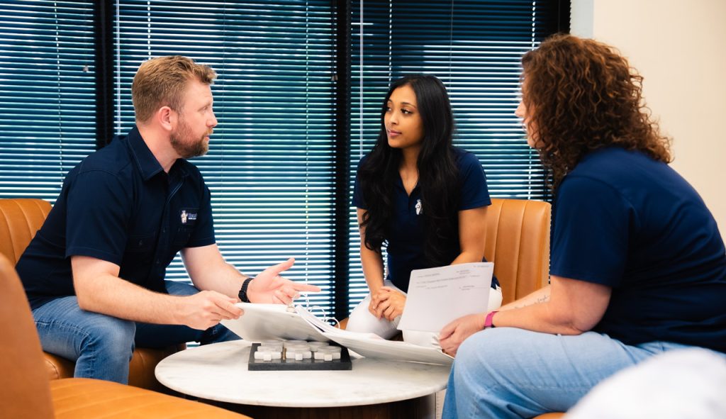 Josh Hembree sitting at a table conferring with two team members, reviewing documents