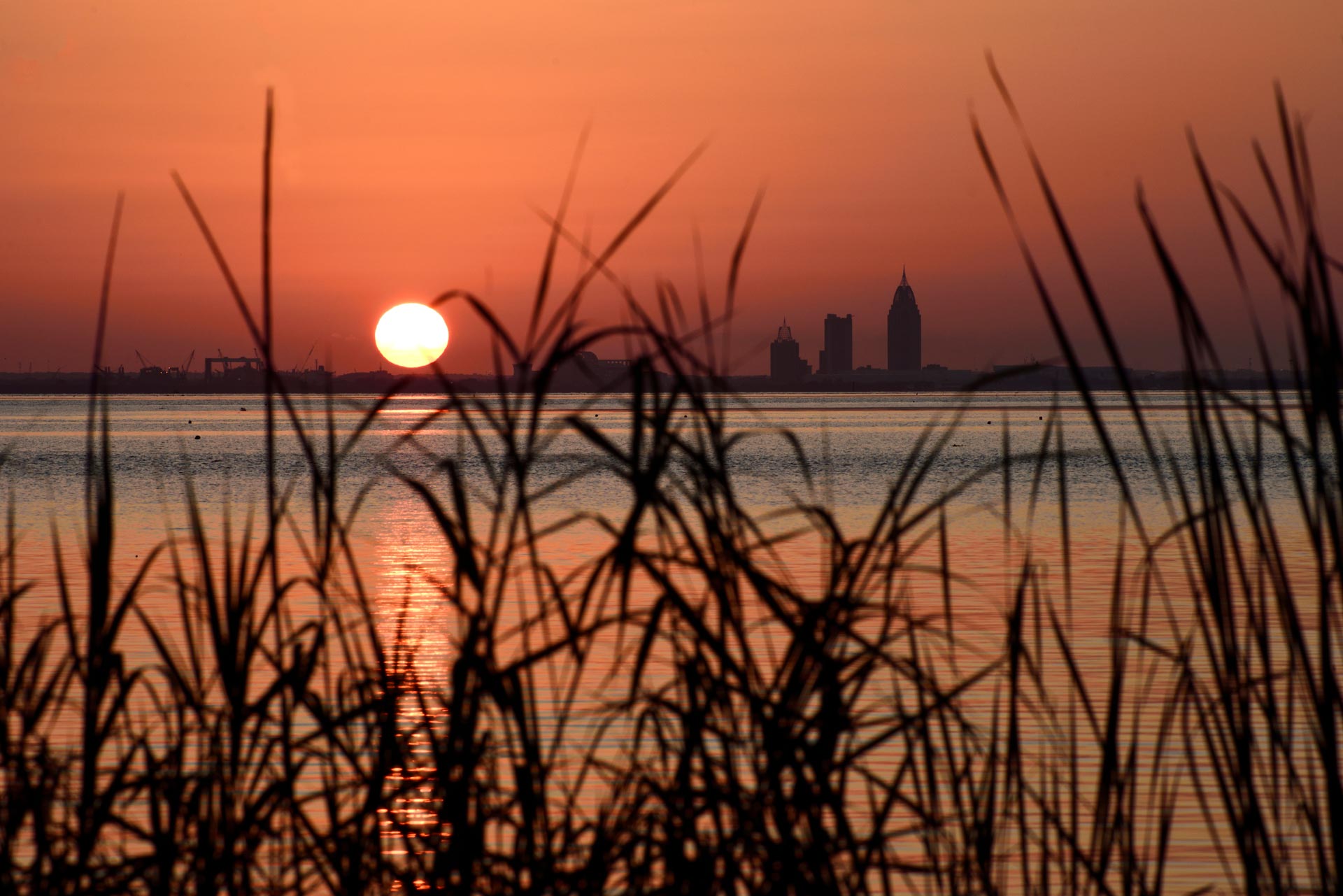 The sun sets over the skyline of Mobile, Alabama, and Mobile Bay as seen from Bayfront Park in Daphne, Alabama, on June 21, 2024.