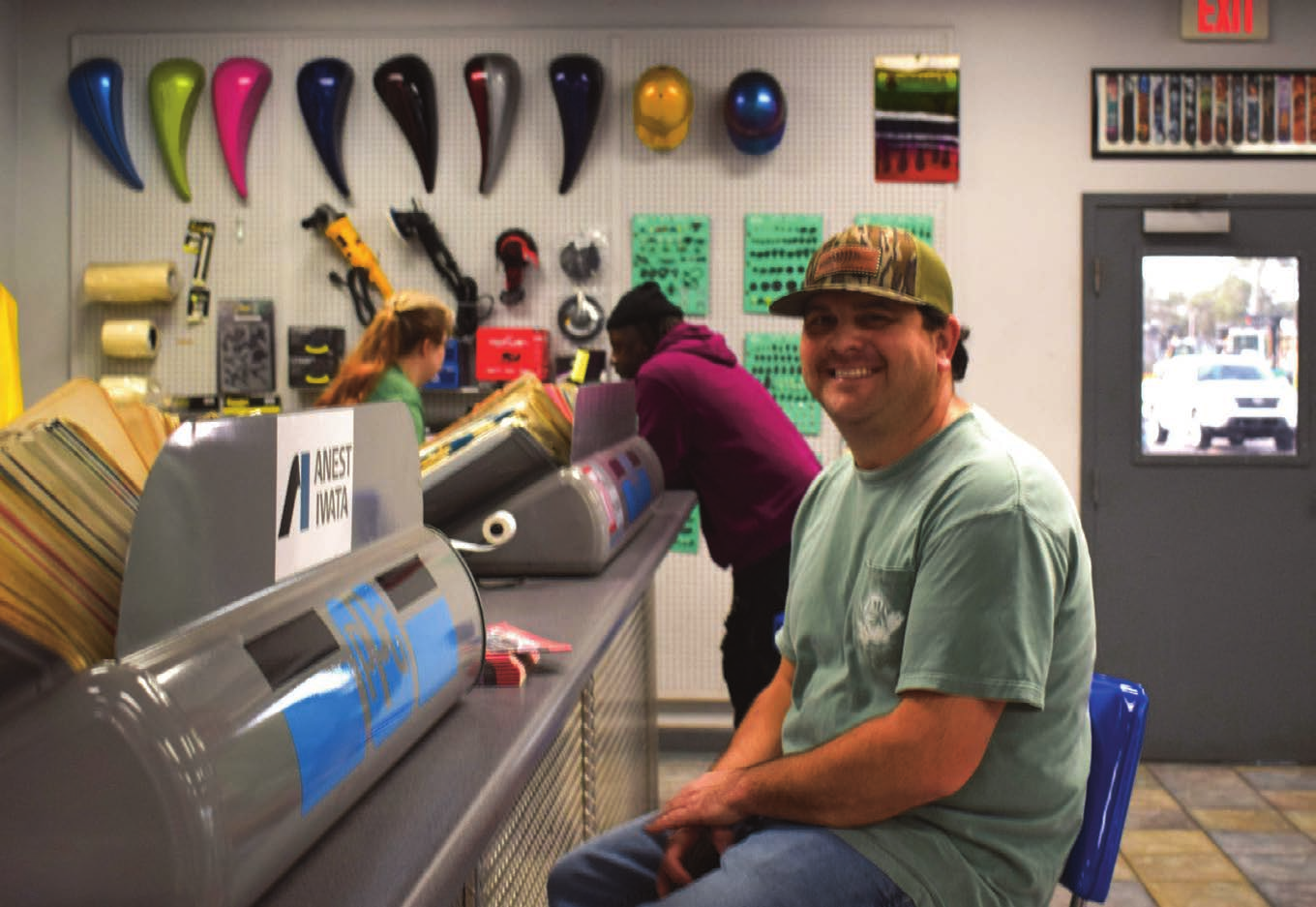 Smiling customer in a cap seated at an APS counter with spray equipment on display behind him