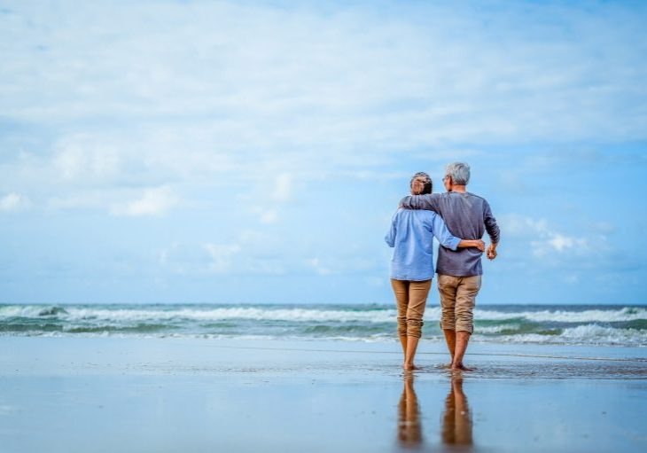 Plan life insurance of happy retirement concepts. Senior couple walking on the beach holding hands at beach sunrise in evening.