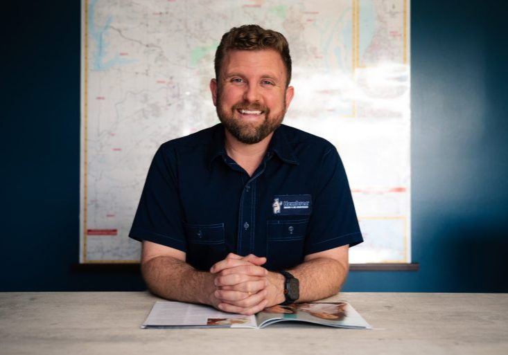 Josh Hembree smiling at desk in Hembree Heating & Air Conditioning uniform, in front of a large map