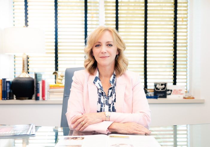 Teresa Williamson seated at her desk in a pink blazer and blue patterned blouse