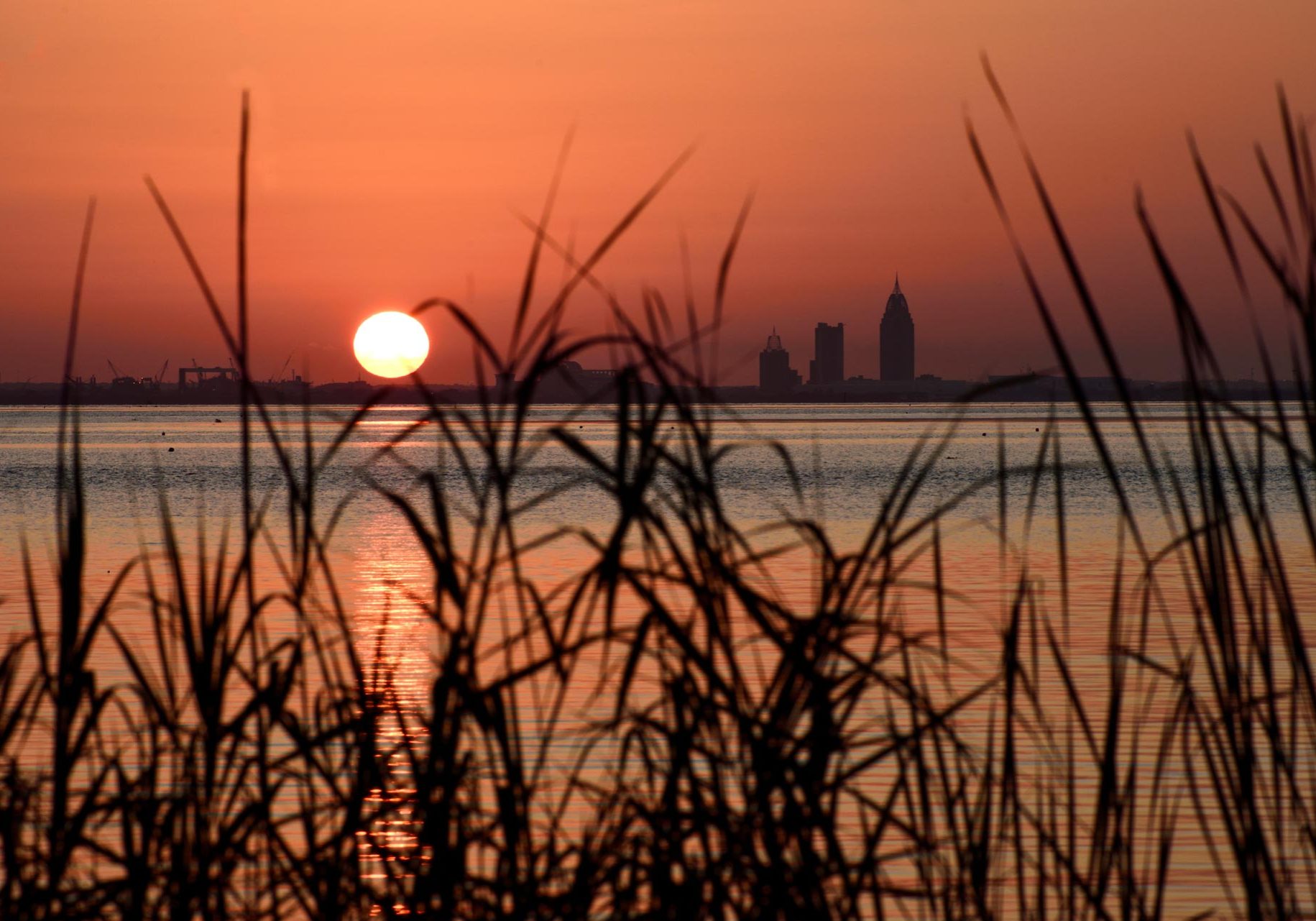 The sun sets over the skyline of Mobile, Alabama, and Mobile Bay as seen from Bayfront Park in Daphne, Alabama, on June 21, 2024.